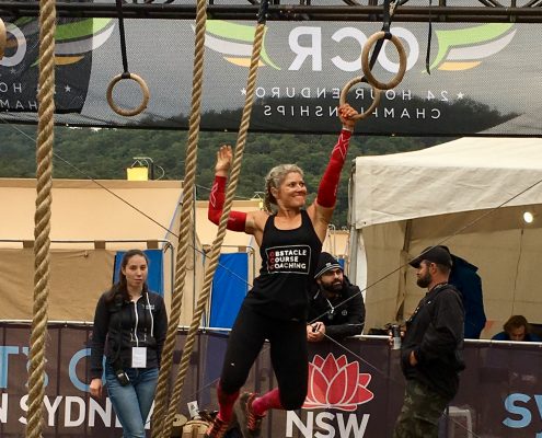 A female athlete competing in a Obstacle Course Race. She is swinging through the rings.