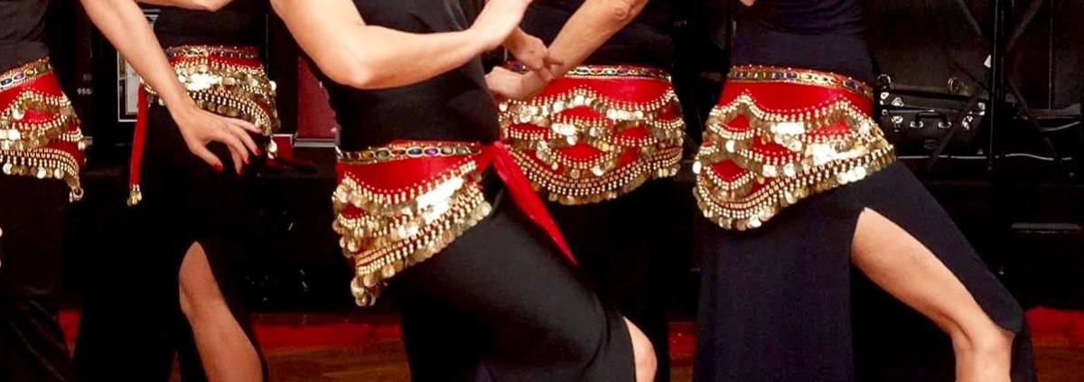 Female dancers dressed in long black gown with red sashes covered in gold coins.